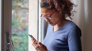 A woman looks at a phone while standing next to a glass door. 