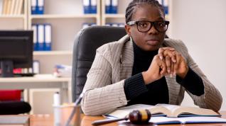 Woman seated at a desk facing the camera, a gavel is on the desk. 